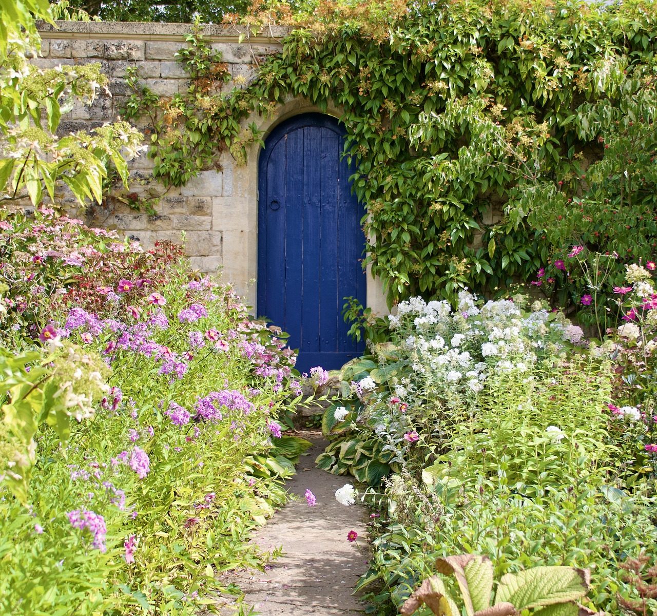 A path through a garden leading to a blue door set in a stone wall.